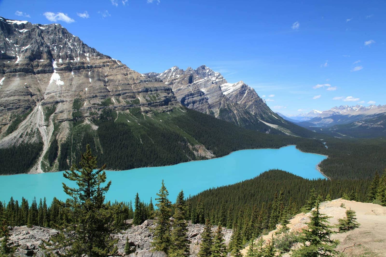 A turquoise mountain lake with forest and peaks.