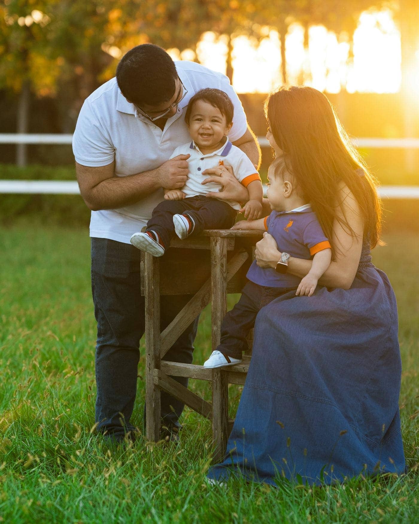 A family outdoors in warm evening light, parents with two young children.