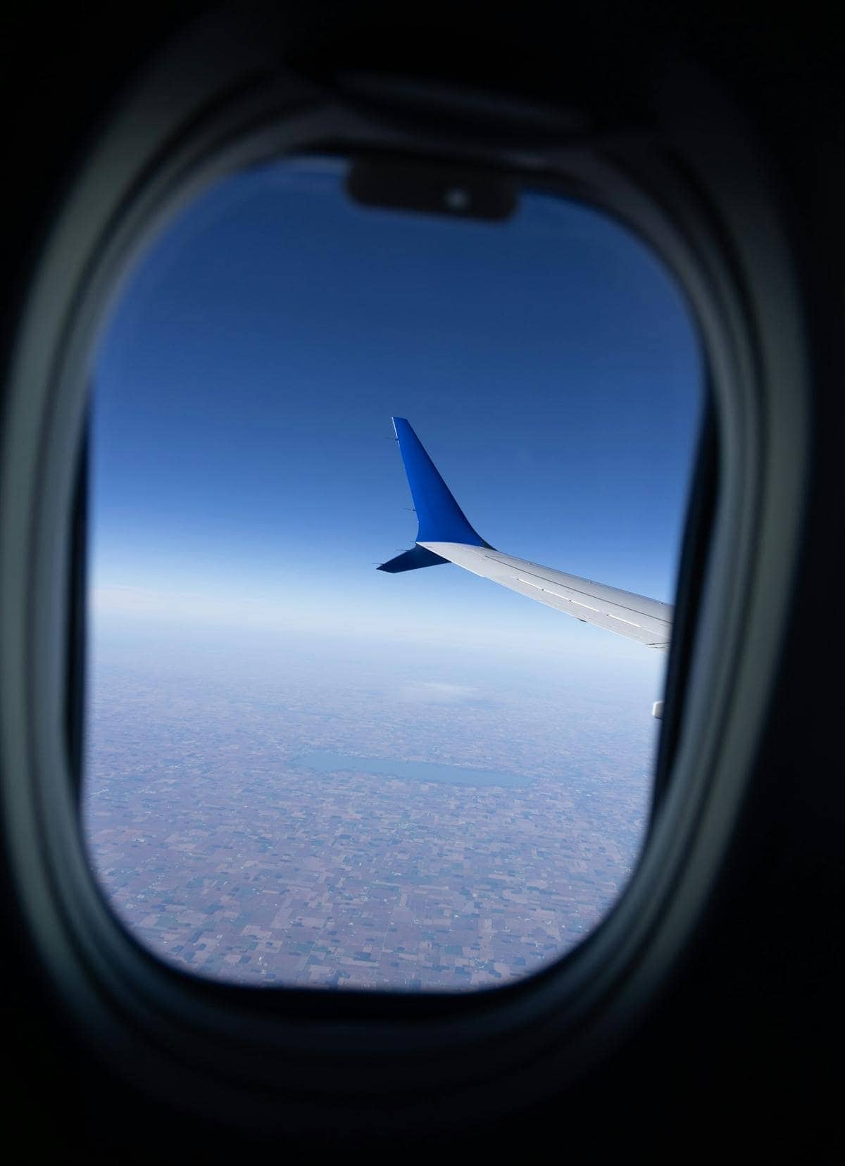 An airplane wing seen through a cabin window above the clouds.